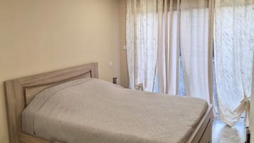 Ein Schlafzimmer mit einem Bettgestell aus Holz, einem Marmorboden und einem Fenster mit gemusterten Vorhängen.