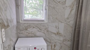 A compact laundry room with a Bosch washing machine, a small window with blinds, and a shower curtain. - Entire Luxury Home (Chalon-sur-Saône)