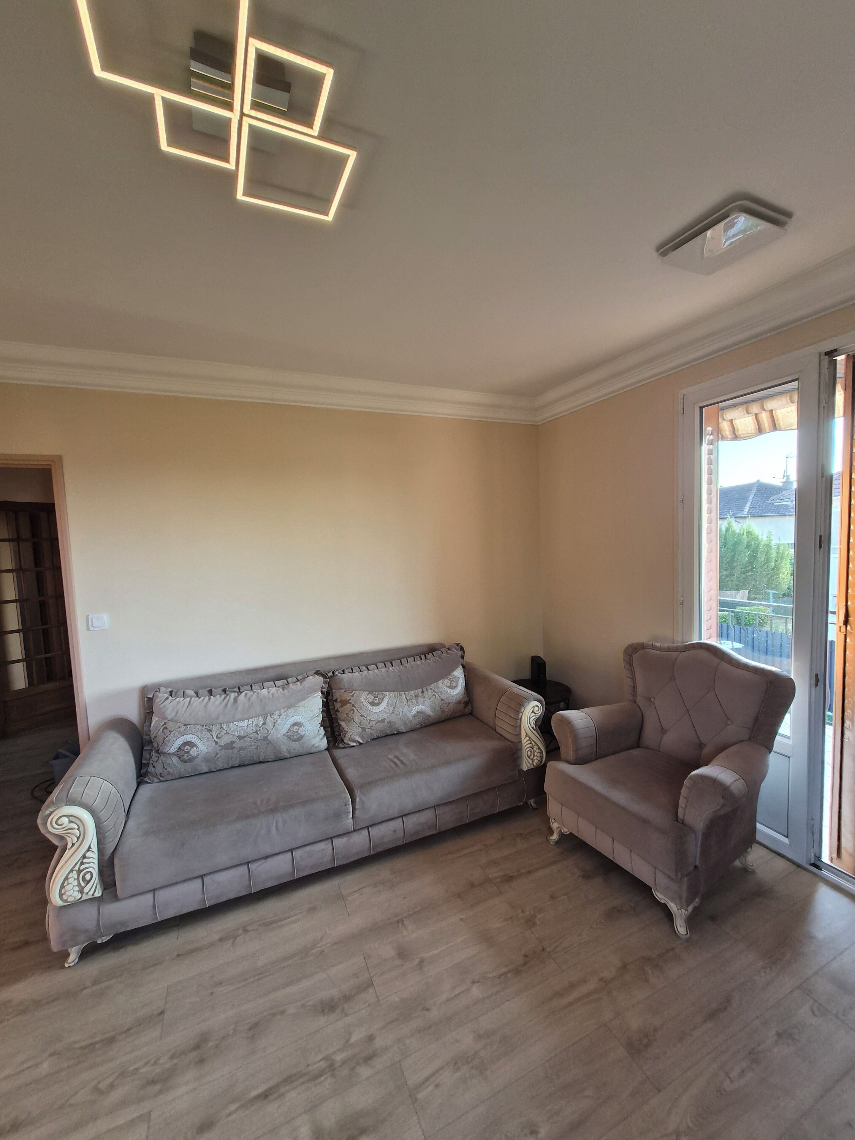 A living room with a sofa and armchair, wooden flooring, and a ceiling light fixture.