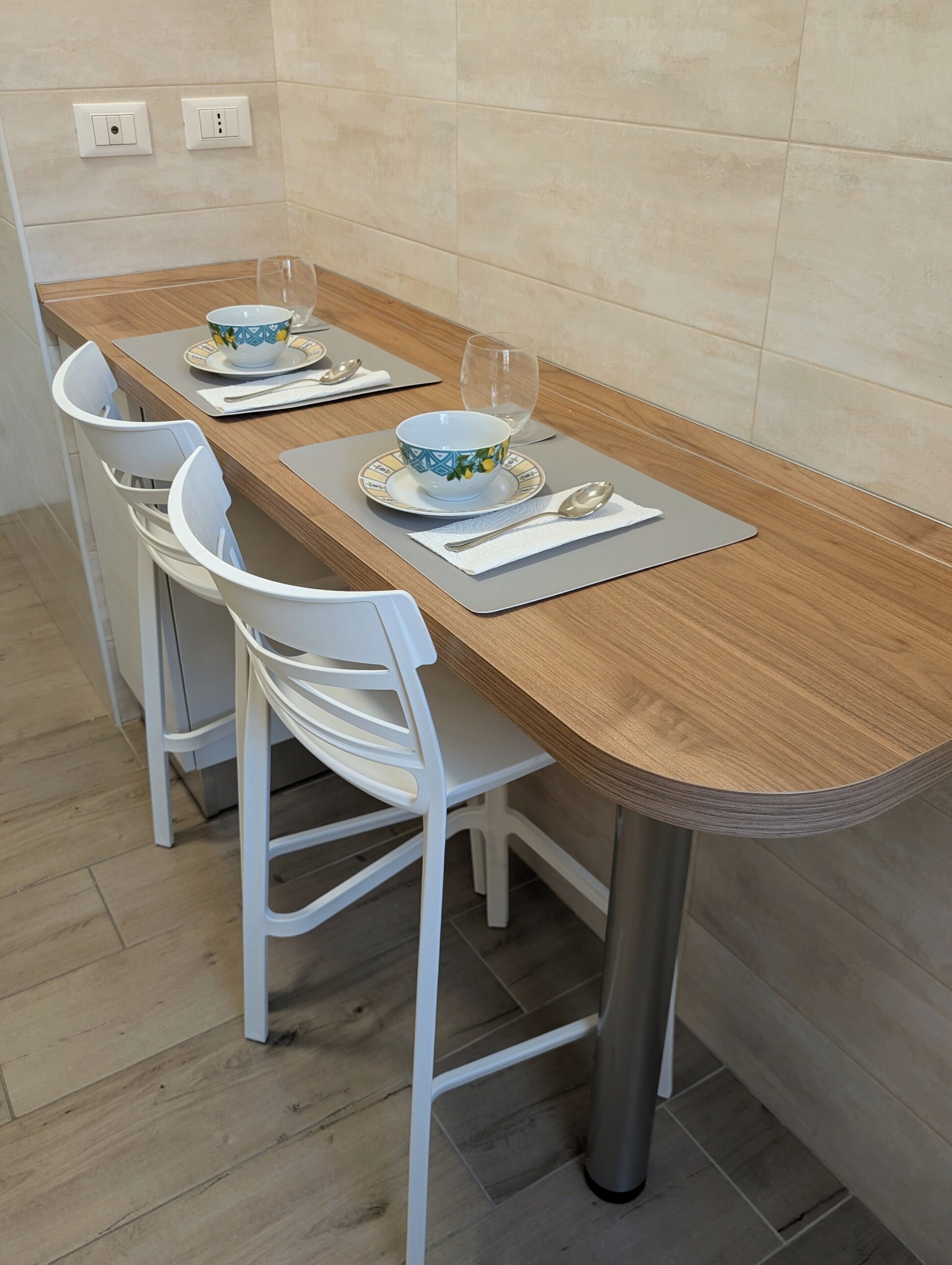A dining table with two chairs, a bowl, a glass, and a spoon on a placemat.