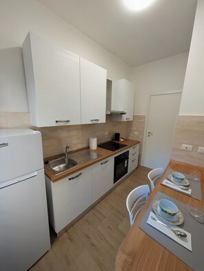 A compact kitchen with white cabinets, a sink, a stove, and a refrigerator. - Lot 235 - Garbatella (Roma)