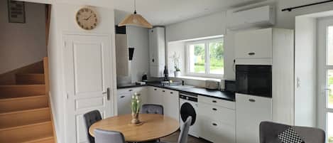 A modern kitchen with white cabinets, a dining table with chairs, a clock on the wall, and a staircase leading to another room.
