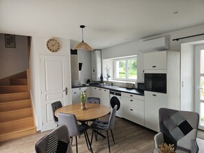 Une cuisine moderne avec des meubles blancs, une table à manger avec des chaises, une horloge au mur et un escalier menant à une autre pièce.