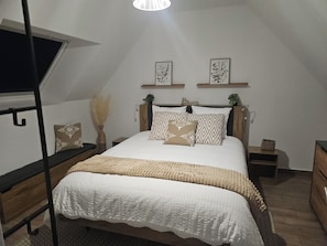A bedroom with a bunk bed, a large bed with patterned pillows, a bedside table with a plant, and a wall-mounted shelf with framed pictures. - Air-conditioned house for 4 people near the beach with a private heated spa (Erdeven)