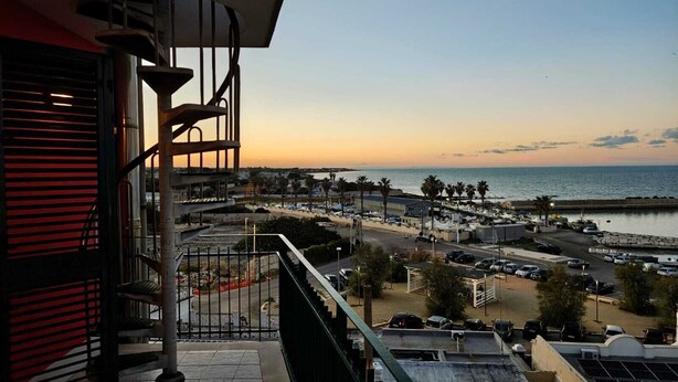 Un balcón con vistas a la costa, que incluye una playa y un paseo marítimo.