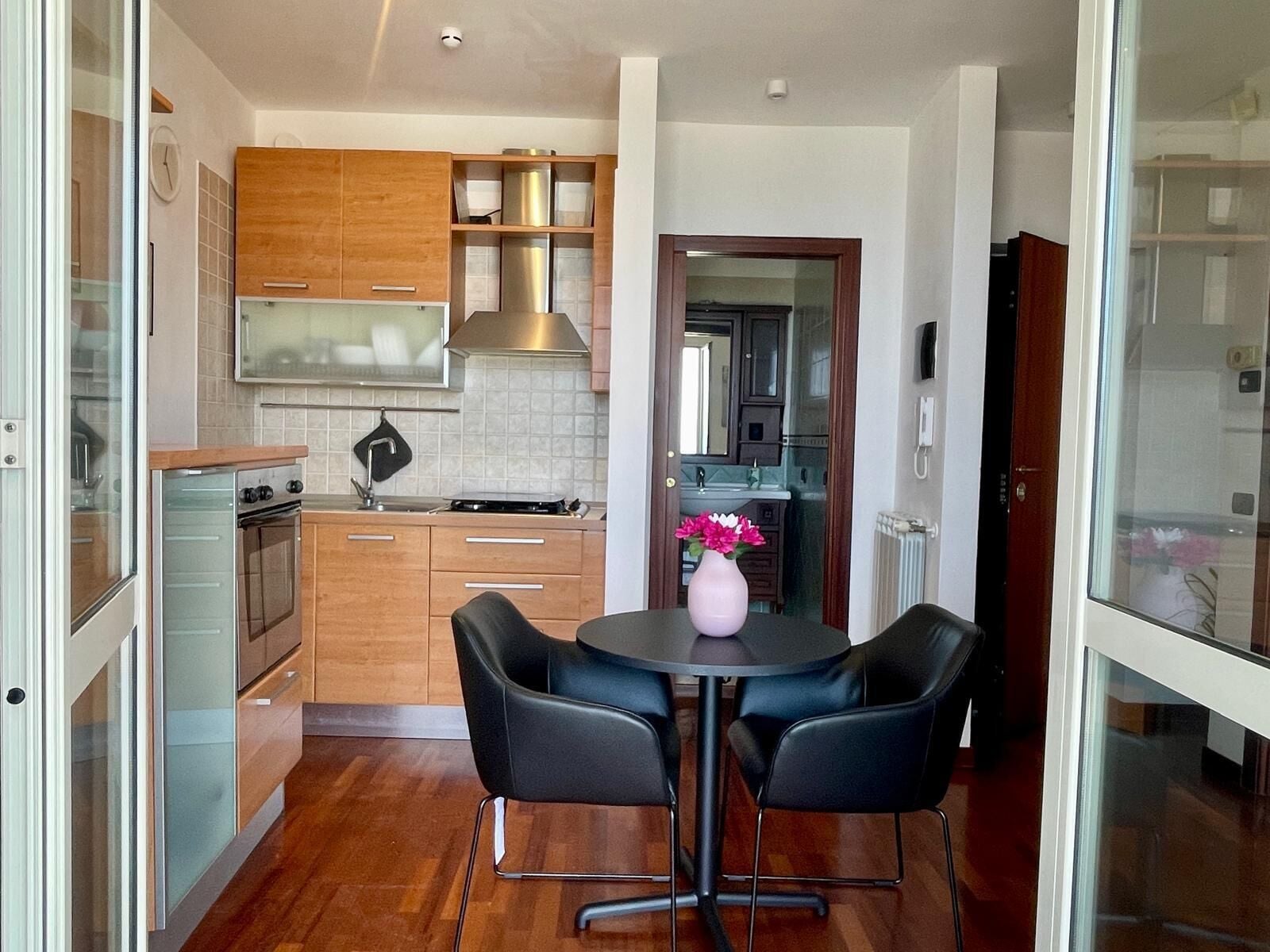 Cocina compacta con electrodomésticos modernos, una mesa de comedor con sillas y vista al baño contiguo.