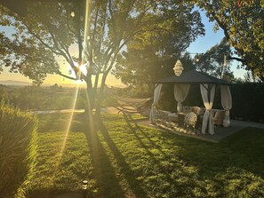 Ein Pavillon mit Schachbrettboden, umgeben von Gras und Bäumen, wobei Sonnenlicht durch das Laub scheint.