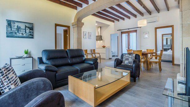 A modern living room with a black leather sofa, a glass coffee table, and a dining area with wooden furniture. - Central House With Pool, Puerto Pollenca (Pollença)