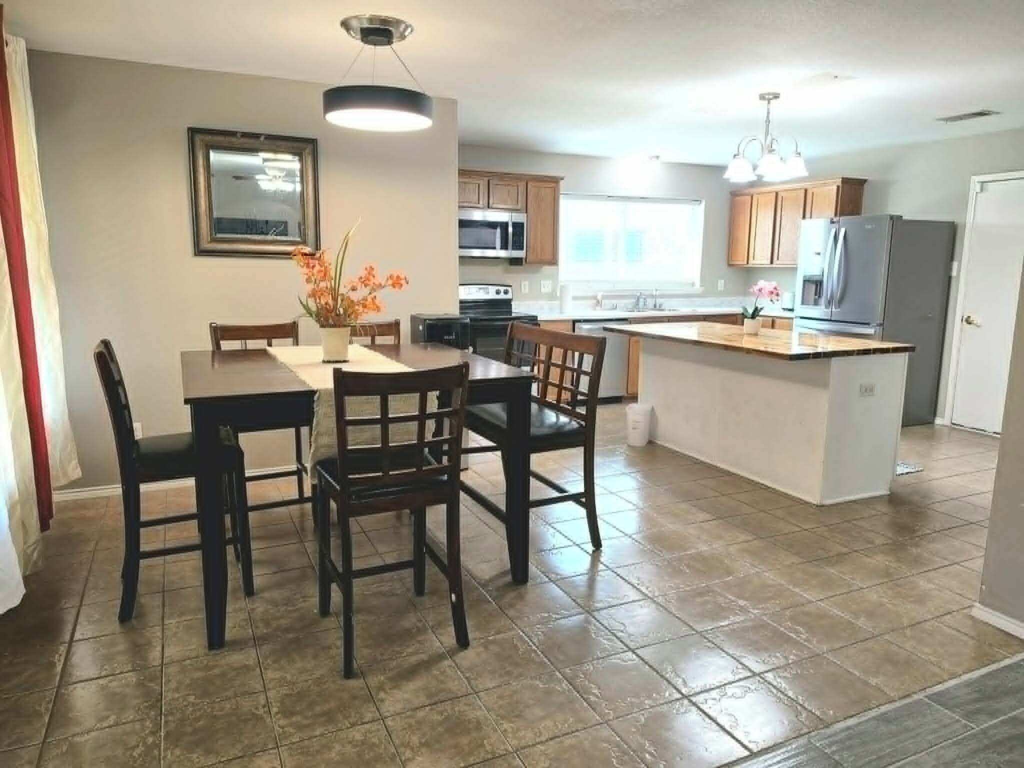 A modern kitchen with a dining area, featuring a central island, built-in appliances, and a pendant light.