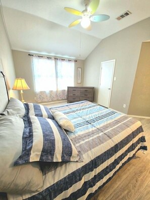 A bedroom with a bed, a dresser, a ceiling fan, and a window with curtains. - Fully Loaded 4BR Cul-de-Sac Home with 3 Living Rooms, Game Room, & big backyard (Fort Worth)