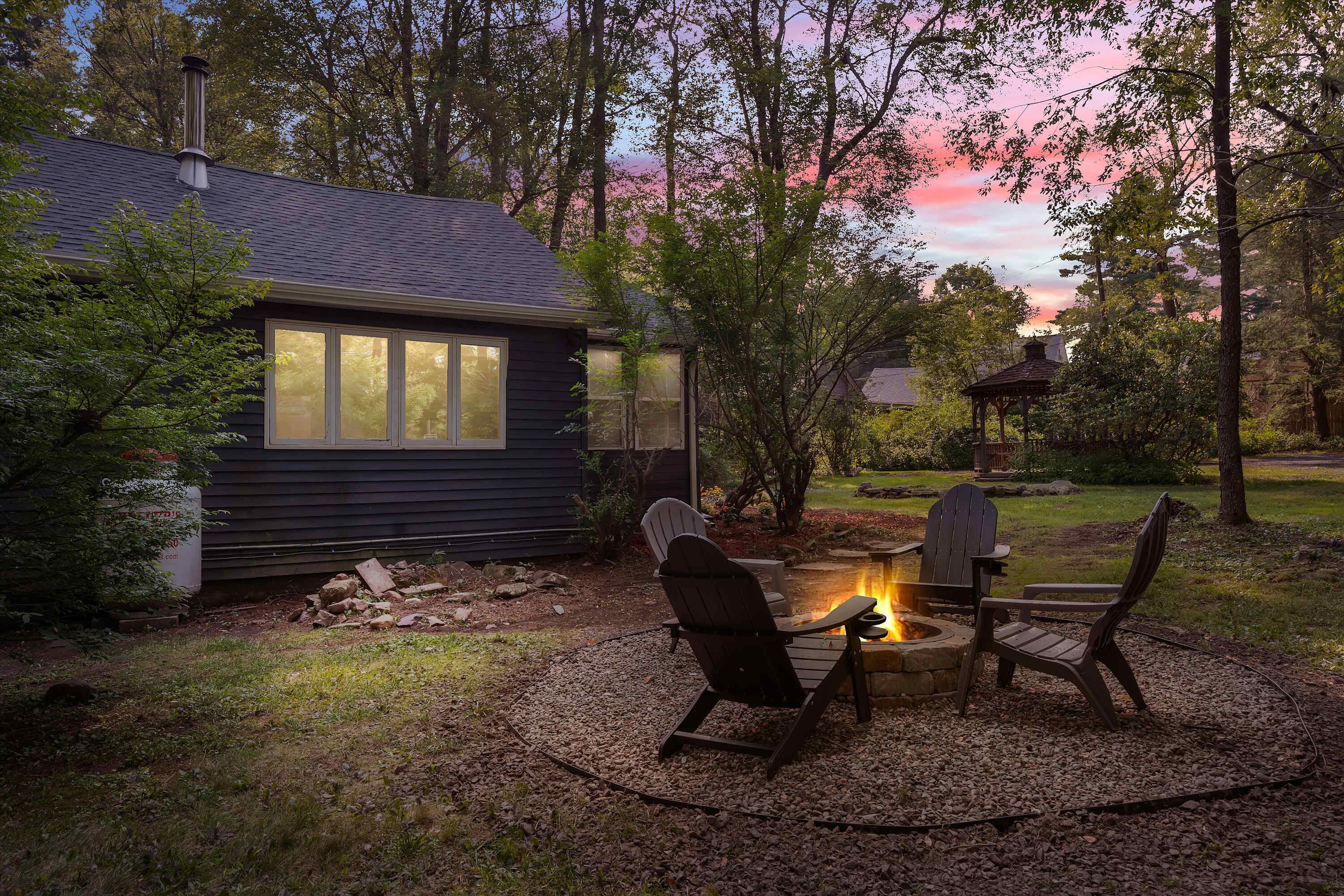 Ein Haus mit Terrasse, Feuerstelle und Adirondack-Stühlen.