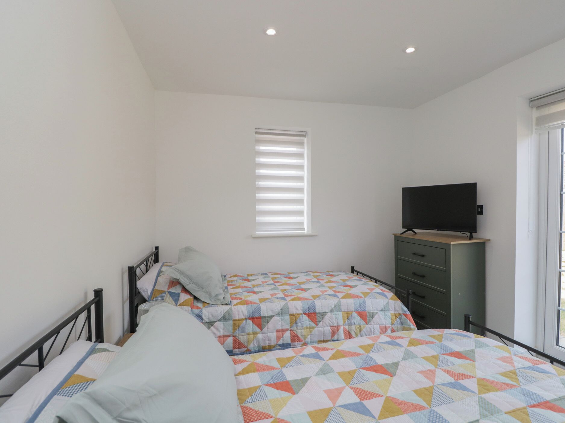 A bedroom with two beds, a television on a dresser, and a window with blinds.