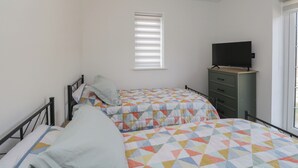 Un dormitorio con dos camas, un televisor sobre un aparador y una ventana con persianas.