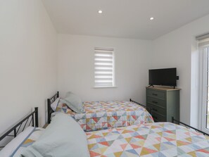 Un dormitorio con dos camas, un televisor sobre un aparador y una ventana con persianas.