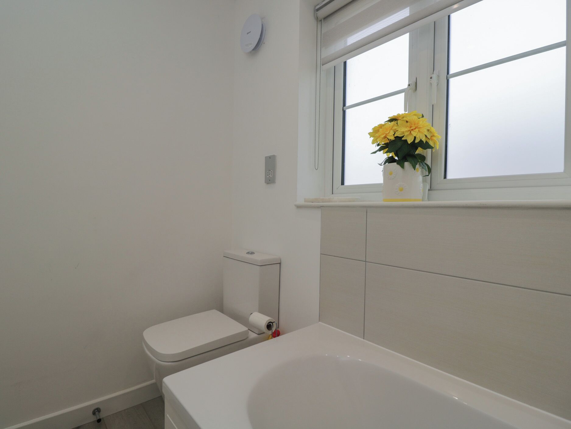 Un baño con inodoro, bañera y una ventana con un florero.