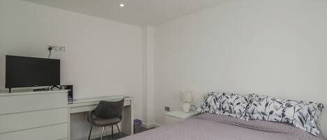 A bedroom with a bed, a desk, a chair, and a television.
