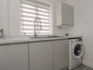 A modern kitchen with a built-in washing machine, a sink, and a window with blinds. - 1 Brunel Court (Marlborough)