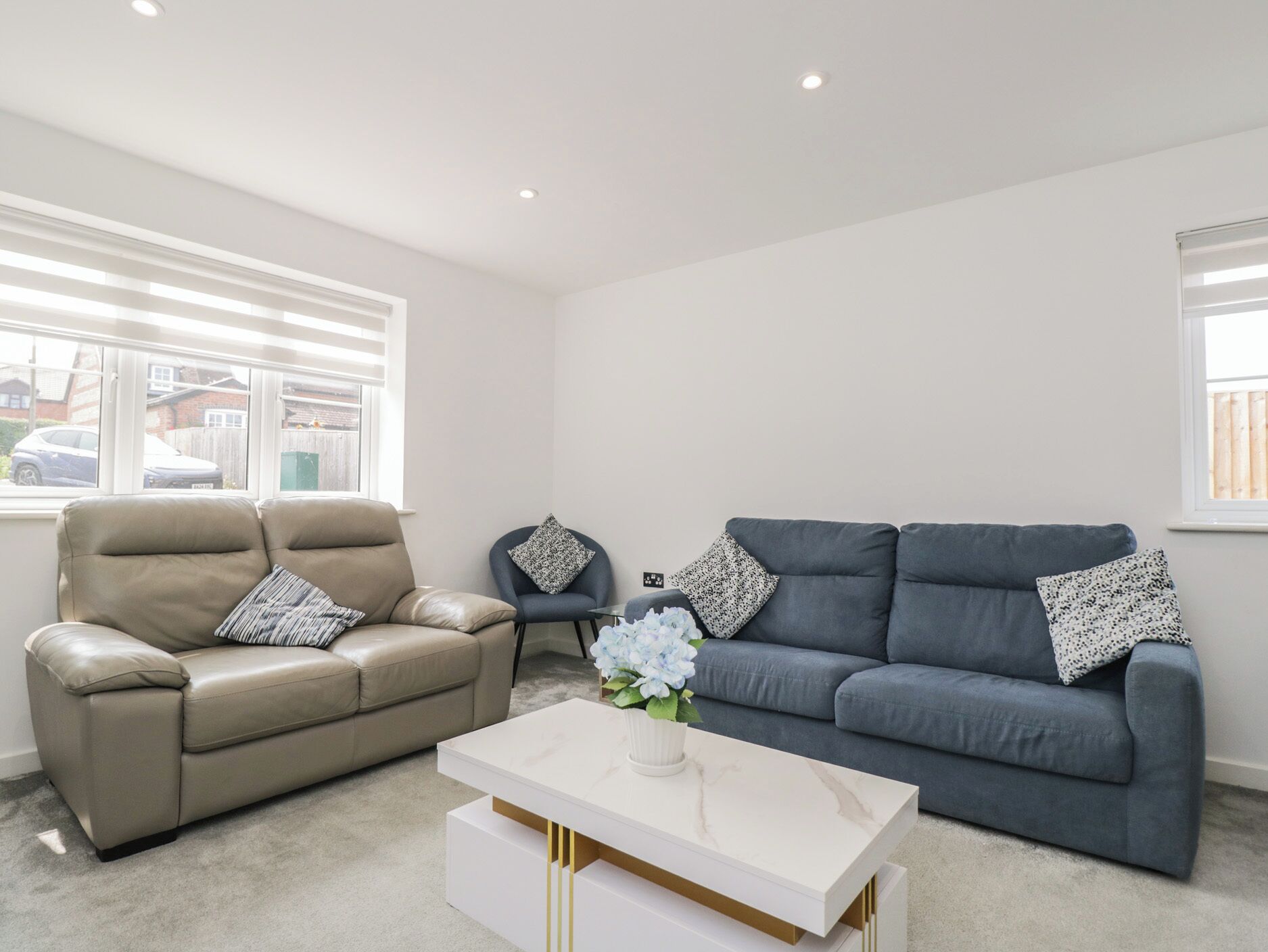 A living room with a beige leather sofa, a blue sofa, and a white coffee table with a vase of flowers.
