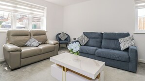 Una sala de estar con un sofá de cuero color beige, un sofá azul y una mesa de centro blanca con un jarrón de flores.