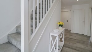 Una escalera con barandas blancas y pasamanos de madera que lleva a un rellano con una consola blanca y un florero de flores amarillas.
