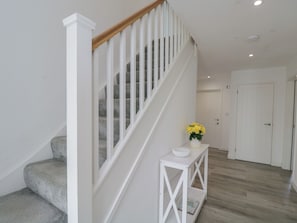 Una escalera con barandas blancas y pasamanos de madera que lleva a un rellano con una consola blanca y un florero de flores amarillas.