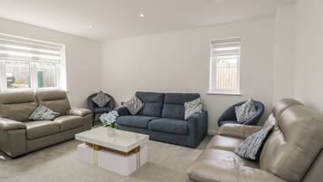 A living room with a beige sofa, a dark blue sofa, and a white coffee table with a vase of flowers.