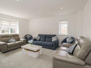 Una sala de estar con un sofá color beige, un sofá azul oscuro y una mesa de centro blanca con un jarrón de flores.