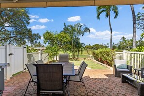 Eine Terrasse im Freien mit Tisch und Stühlen, umgeben von einem weißen Zaun, Palmen und einem wolkenlosen Himmel.