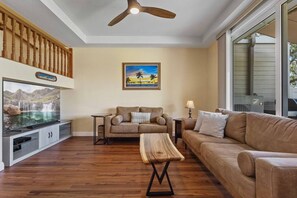 A living room with a flat-screen TV, a wooden coffee table, a beige sofa, and a ceiling fan. - Wake Up to Golf Course Views & Resort Amenities (Kapolei)