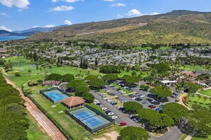 A residential area with a tennis court, parking lot, and a view of mountains. - Wake Up to Golf Course Views & Resort Amenities (Kapolei)