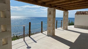Ein überdachter Außenbereich mit Blick auf das Meer, mit Fliesenboden und Holzsäulen.