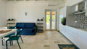 Eine moderne Küche mit weißen Schränken und einer gemusterten Spritzschutzwand, ein blaues Sofa sowie ein Essbereich mit einem weißen Tisch und grünen Stühlen.