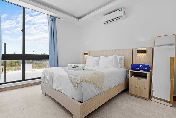Ein modernes Schlafzimmer mit einem großen Bett, einem Nachttisch, einem Spiegel und einer Klimaanlage.