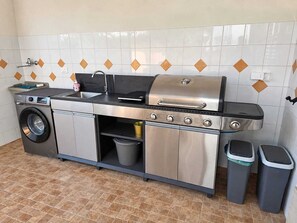 Ett kompakt kök med tvättmaskin, diskho, grill och sopkärl.