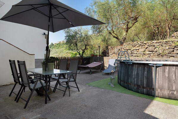 Una terrazza esterna con tavolo e sedie, un ombrellone grande, una vasca idromassaggio e un muro in pietra.