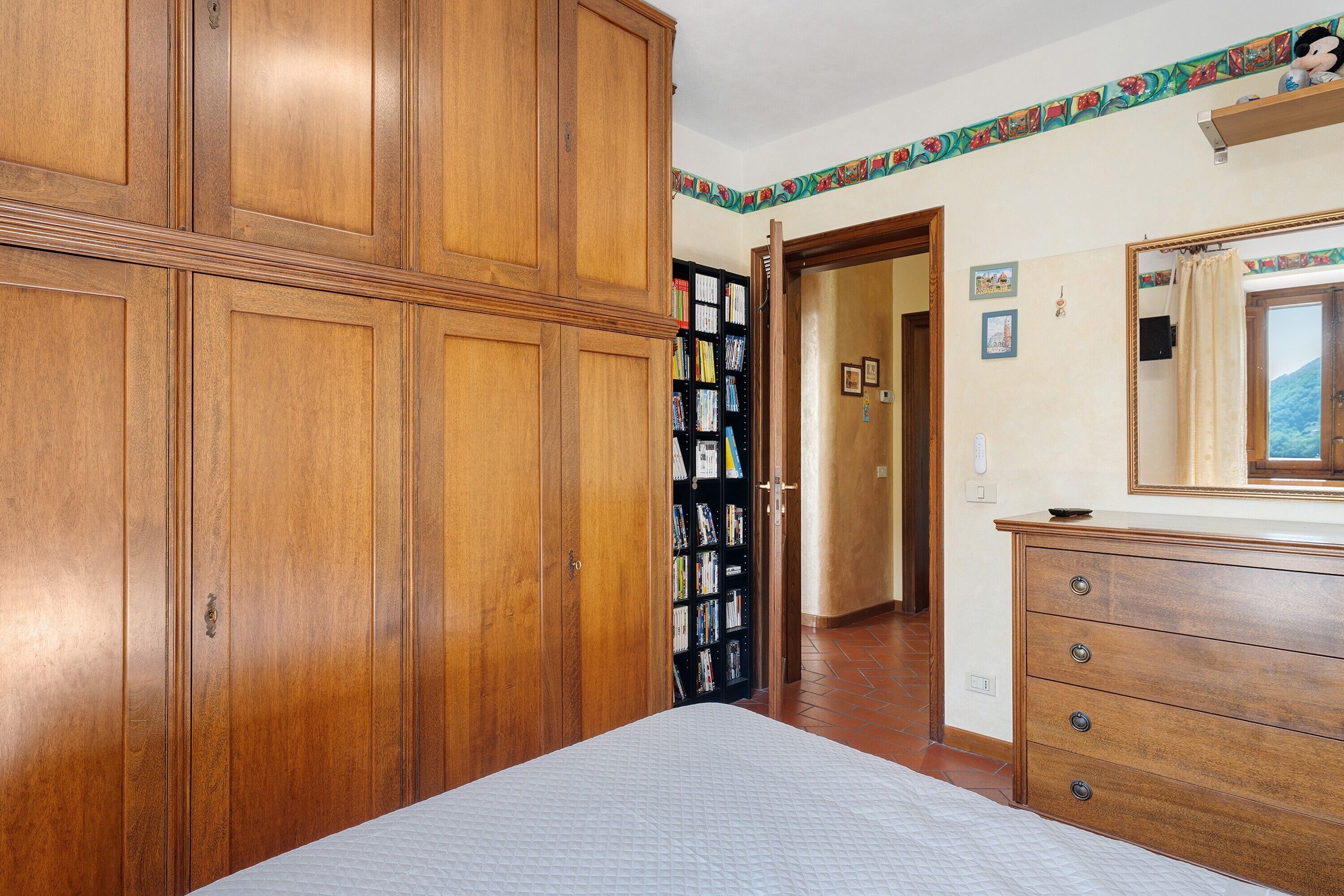 Une chambre à coucher avec une grande armoire en bois, une table de chevet et un miroir.