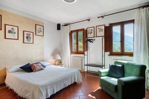 Una camera da letto con un letto, una sedia, un termosifone e stampe botaniche incorniciate alle pareti.
