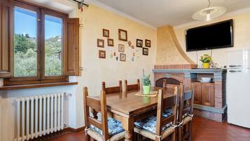 Un coin repas avec une table et des chaises en bois, une cuisine équipée d’un téléviseur et une fenêtre donnant sur un paysage verdoyant.