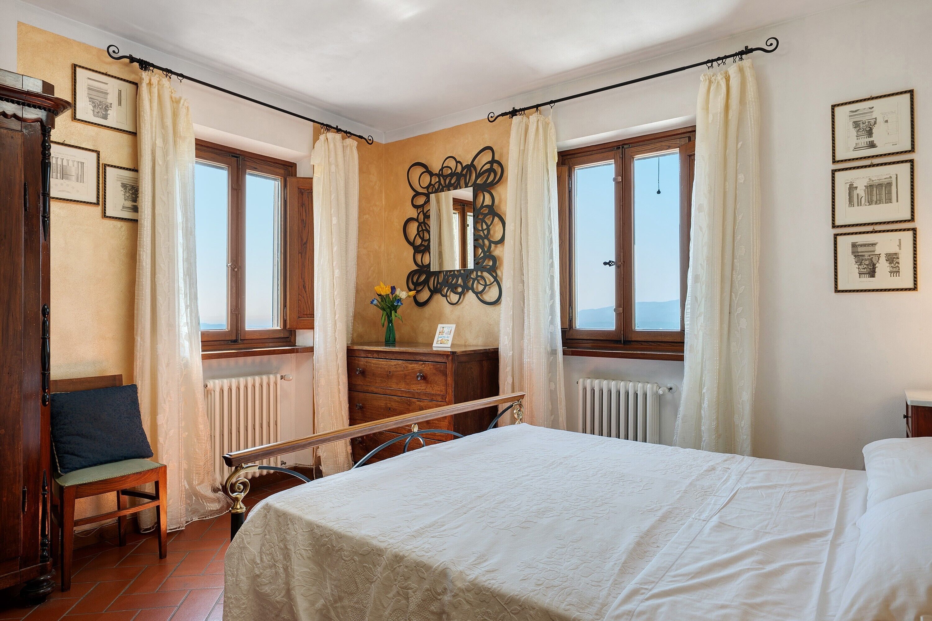 Une chambre à coucher avec un lit, une commode, un miroir et une fenêtre avec des rideaux.