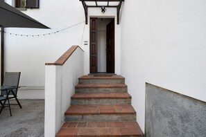 A set of outdoor brick stairs leading to a dark wooden door, a small outdoor table with a chair, and a string of lights above. - Alla Polla Relax near Lucca: Mountain View, Private Pool, Wi-Fi (Matraia)