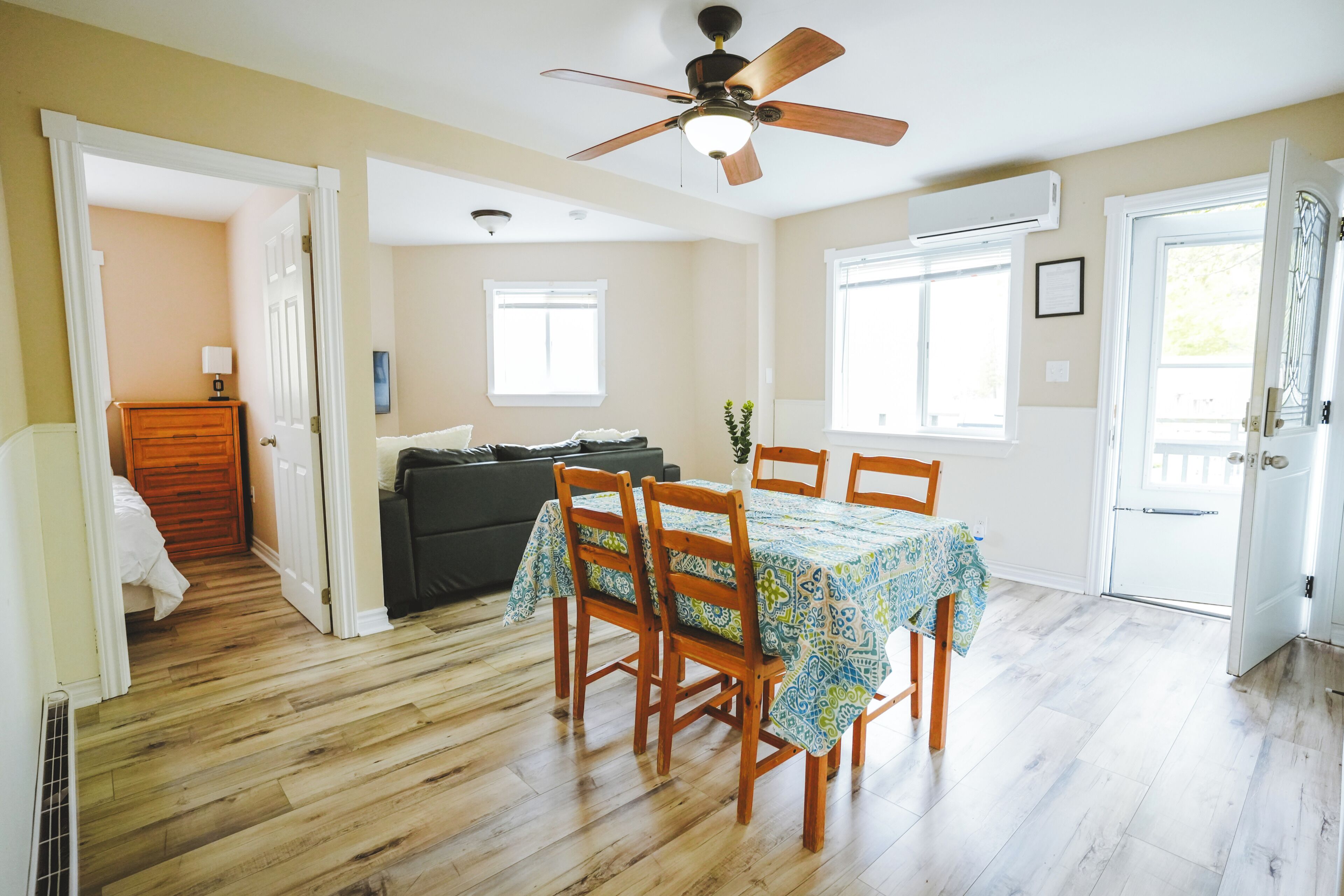 A dining area with a table set for four, wooden chairs, a ceiling fan, and a view of a living room through an open door.
