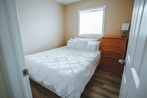 A bedroom with a bed, a nightstand, a window with blinds, and a door.