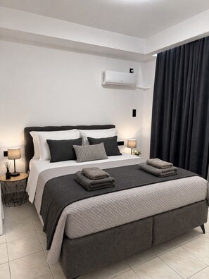 Un dormitorio moderno con una cama grande, lámparas de noche, aire acondicionado instalado en la pared y una cortina oscura.