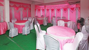 A banquet hall with round tables covered in pink tablecloths and white chairs, a green carpet, and pink drapery on the walls. - Townhouse Hatia Railway Station (Ranchi)