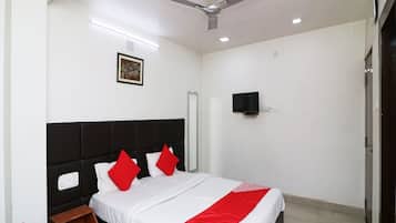 A hotel room with a bed, a ceiling fan, a mounted TV, and a framed picture on the wall.