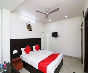 Ein Hotelzimmer mit einem Bett, einem Deckenventilator, einem angebrachten Fernseher und einem gerahmten Bild an der Wand.