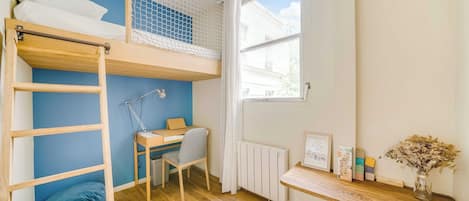 A room with a bunk bed, desk, chair, radiator, window, and a small shelf with items.