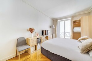 Une chambre à coucher comprenant un lit, une chaise, un bureau avec une télévision, une armoire et une fenêtre donnant sur un balcon.