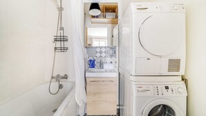 Une petite salle de bain avec une douche, un lave-linge et un sèche-linge superposés, et un mur recouvert de carreaux décoratifs.