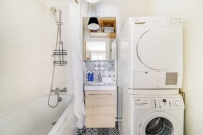 Ein kleines Badezimmer mit Dusche, untergestellter Waschmaschine und Trockner sowie einer Wandfliesenverkleidung mit Muster.